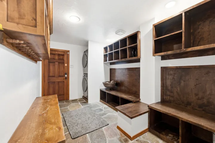 Mudroom featuring stone flooring, built-in wooden cabinetry, integrated shelving, and a stacked washer and dryer unit