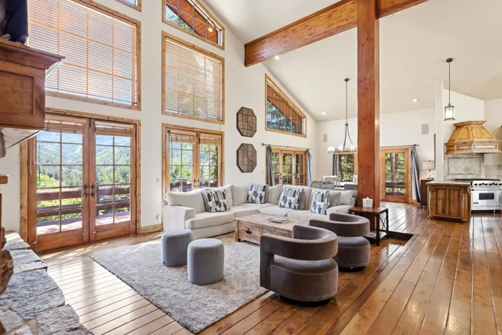 Great room featuring vaulted ceilings, exposed wood beams, hardwood flooring, a stone-front fireplace, and French doors opening to outdoor scenery