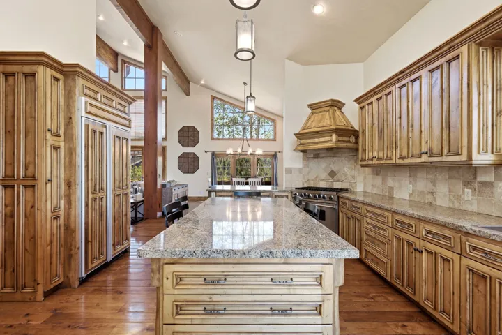 Spacious kitchen featuring an expansive center island, granite countertops, custom wood cabinetry, stainless steel range, and stone tile backsplash