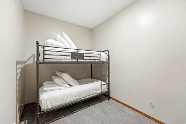 Compact room featuring a metal bunk bed frame, neutral-toned walls, and grey carpeting