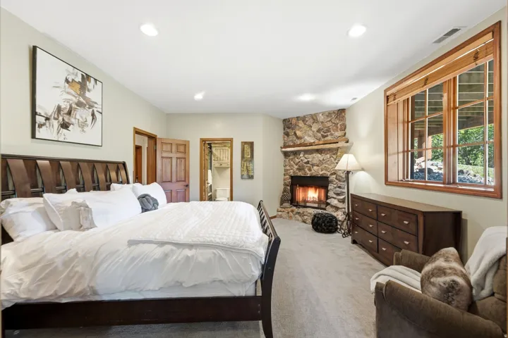 Spacious room featuring a corner stone fireplace, wood-framed windows, recessed lighting, and light-toned carpeting