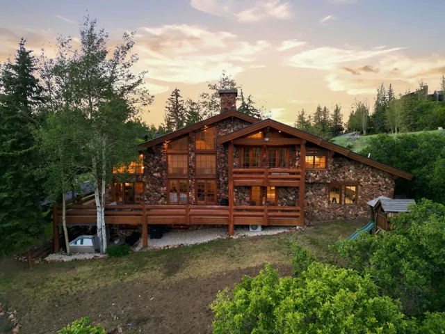 Stone and wood-sided exterior featuring multiple balconies, a large deck, a built-in hot tub, and mature trees
