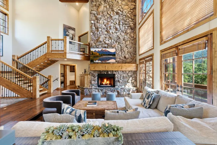 Spacious room featuring a towering stone fireplace, high ceilings, and a grand wooden staircase with wrought iron balusters