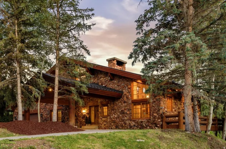 Stone exterior residence featuring a prominent stone chimney, a covered entry with exposed wood beams, and multiple windows with wood frames