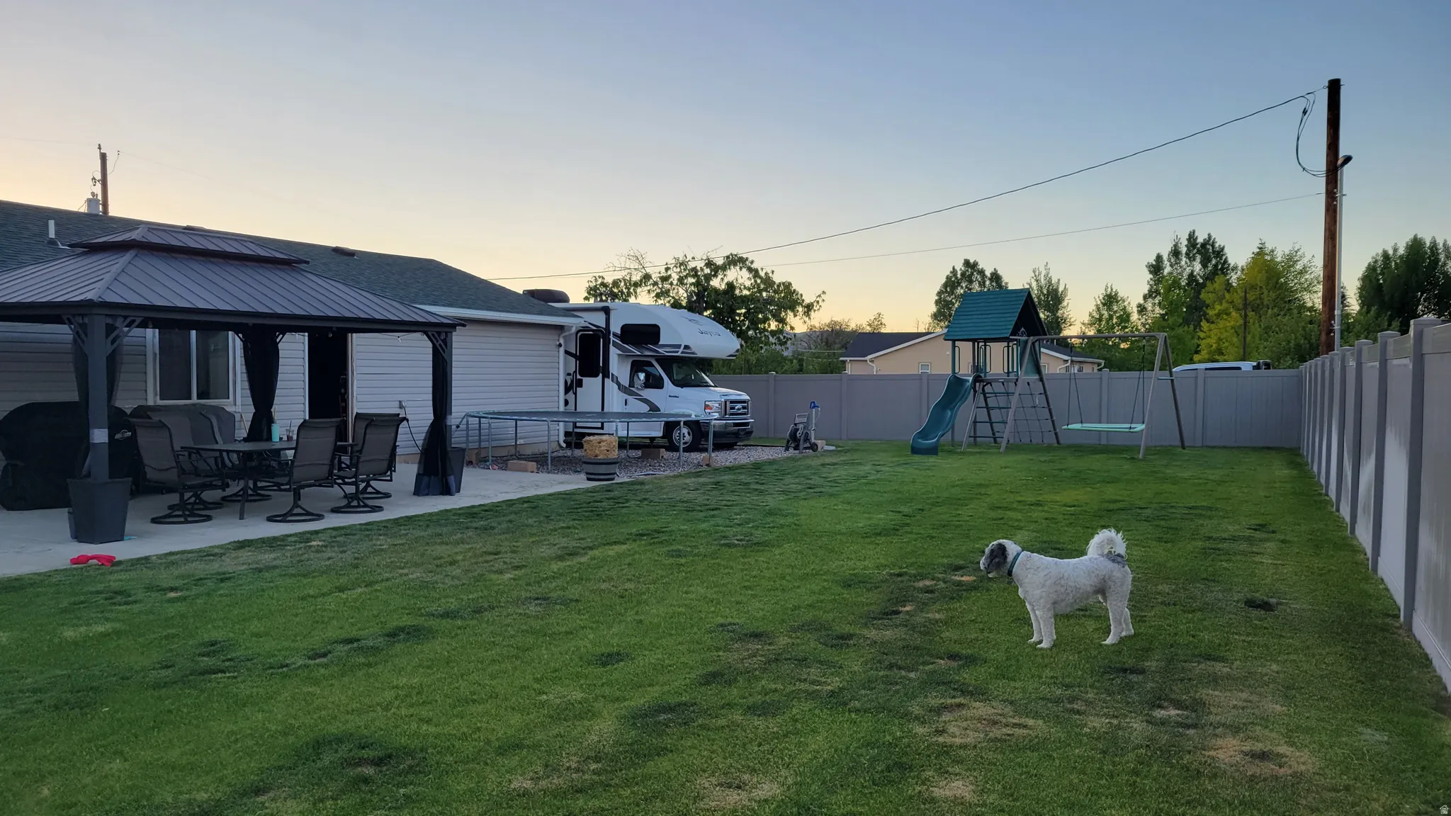 Expansive backyard featuring a manicured lawn, a large patio area with a gazebo, and a privacy fence