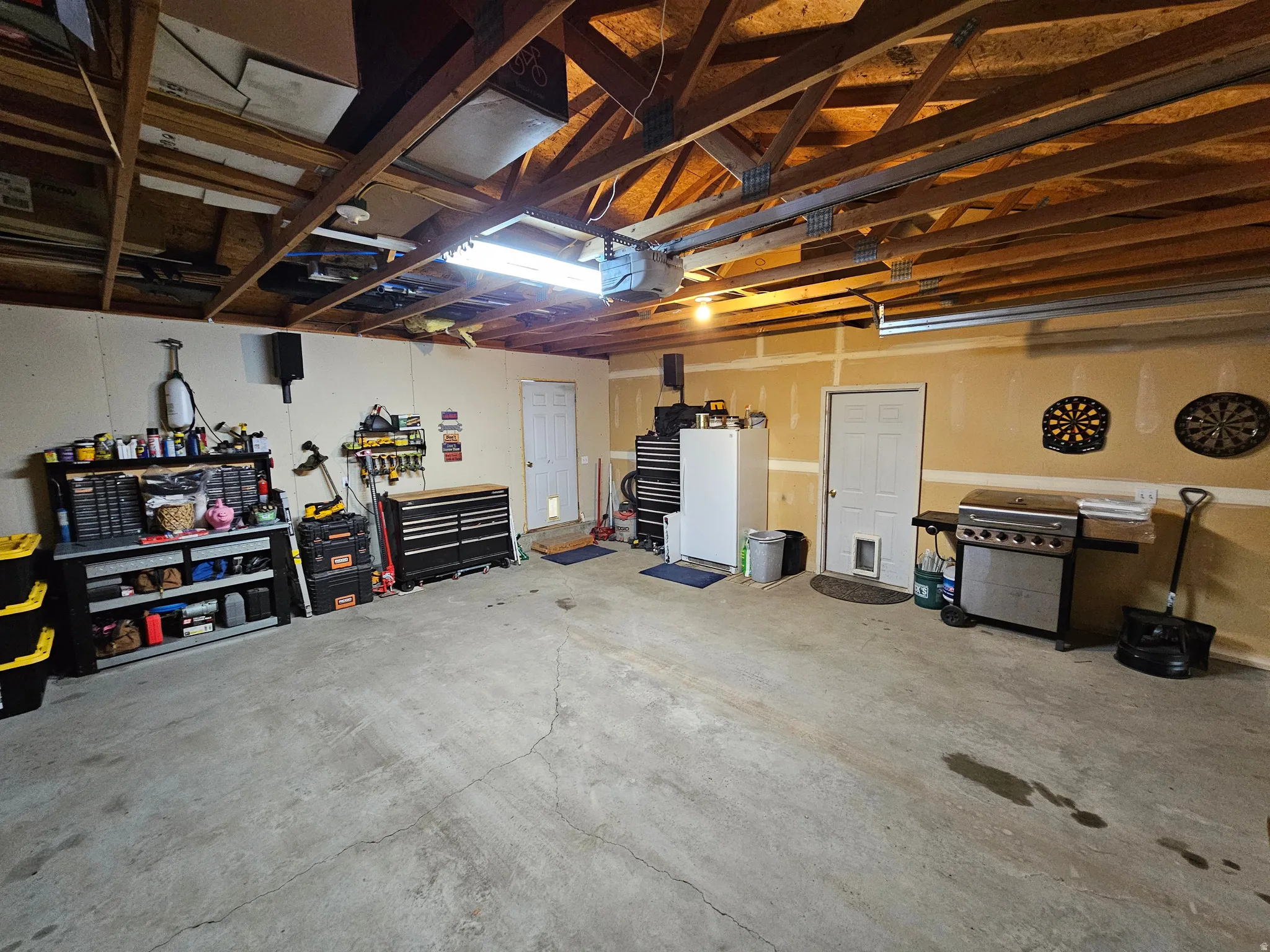 Spacious garage featuring exposed wood beam ceiling, concrete flooring, and multiple access doors