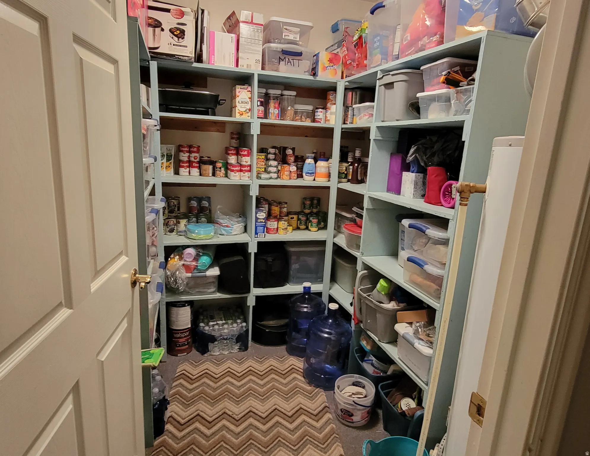 Spacious walk-in pantry featuring extensive built-in shelving, a light-colored solid door, and a chevron-patterned floor covering