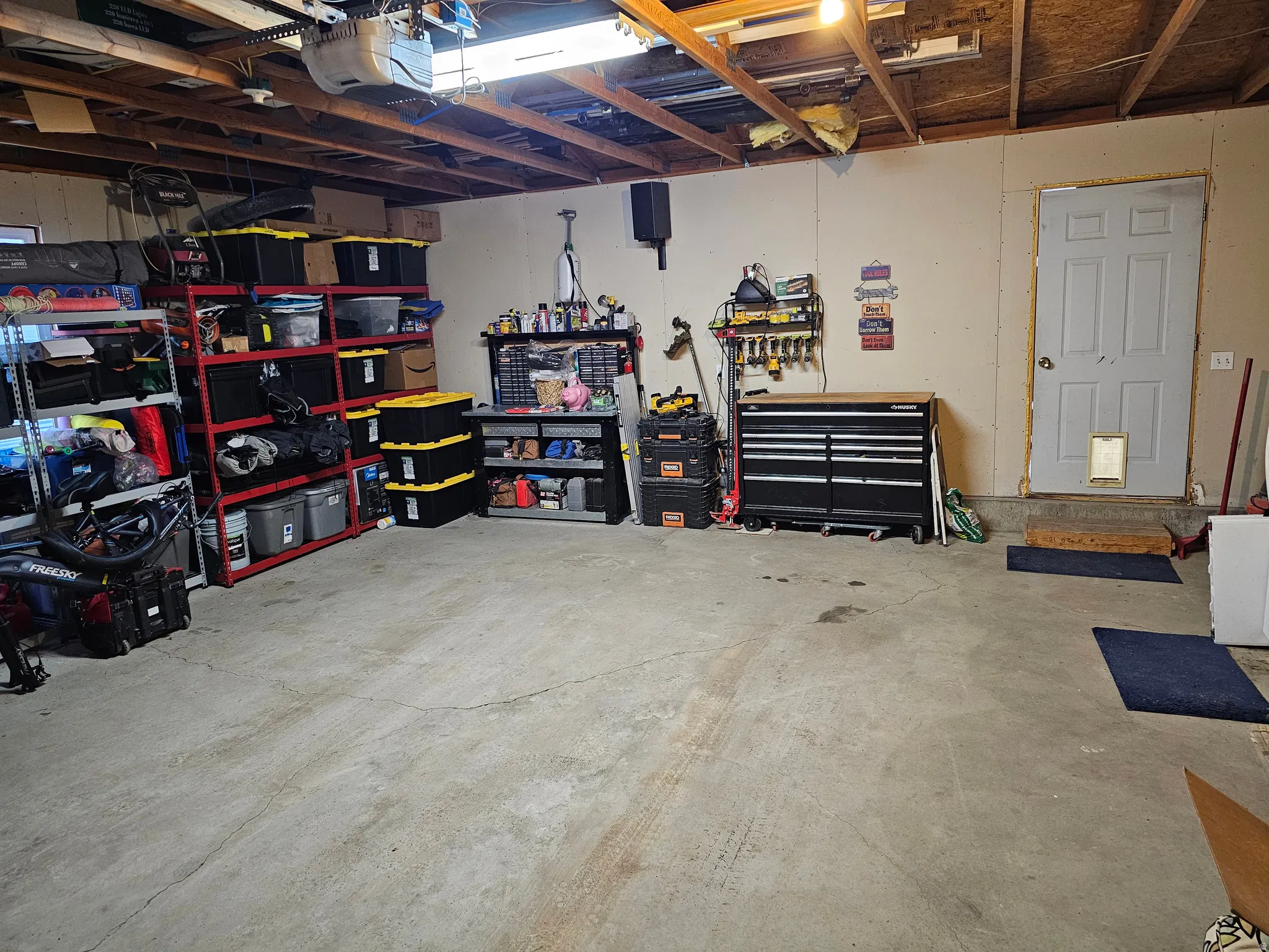 Spacious garage with exposed beam ceiling, concrete flooring, and an overhead garage door opener mechanism