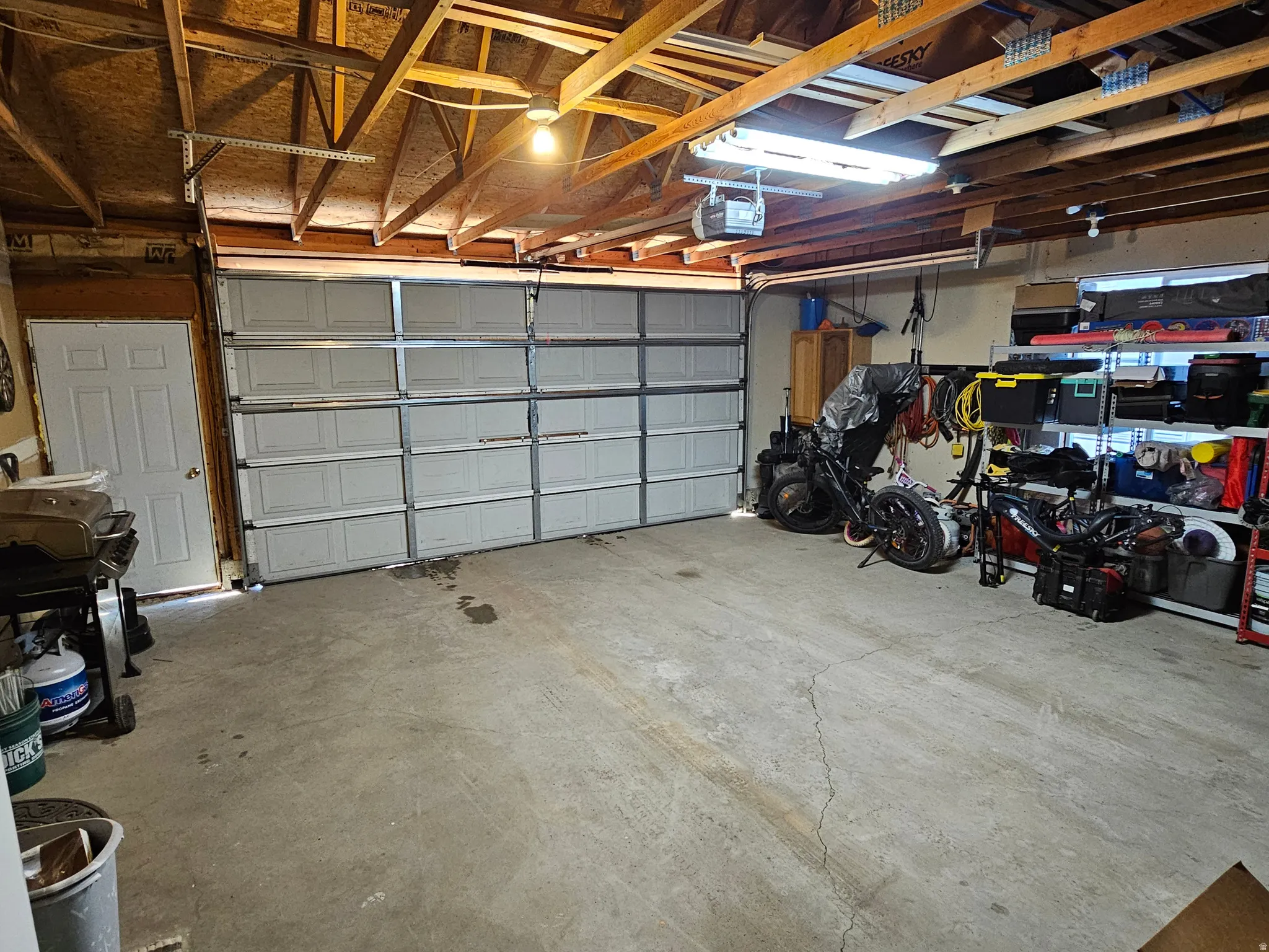 Spacious garage featuring a large paneled overhead door, concrete flooring, exposed wood beam ceiling, and a single paneled entry door