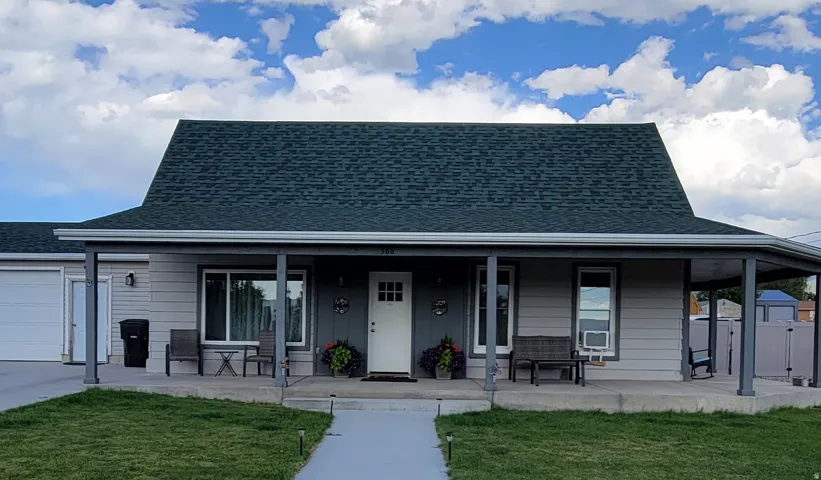 Gabled roofline with dark shingles, covered front porch, light gray siding, white front door with lites, and an attached garage with a white door