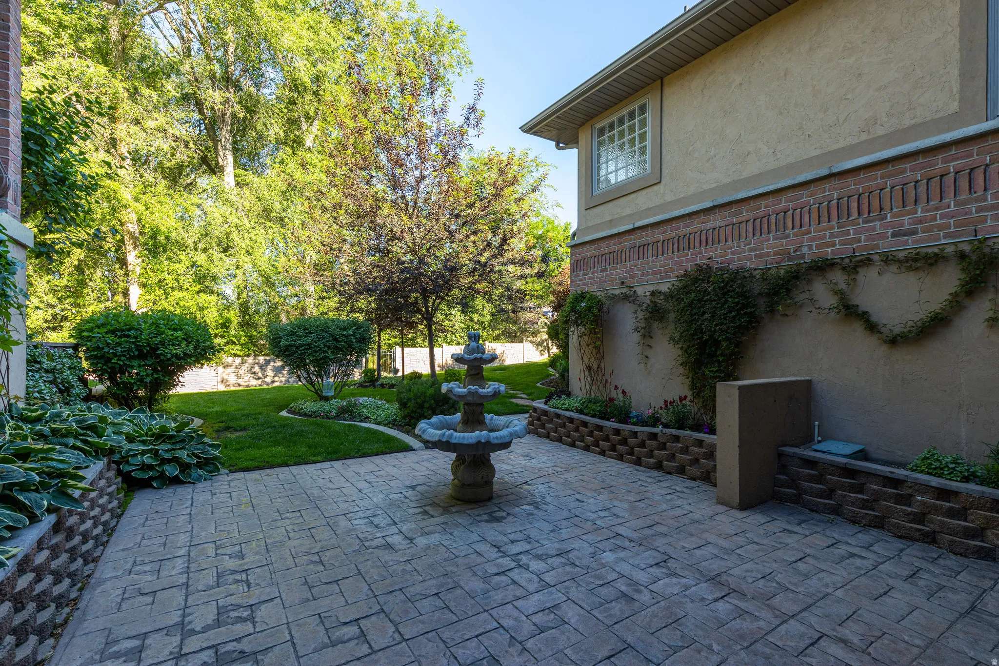 Stamped concrete patio featuring a tiered fountain, bordered by retaining walls with lush plantings