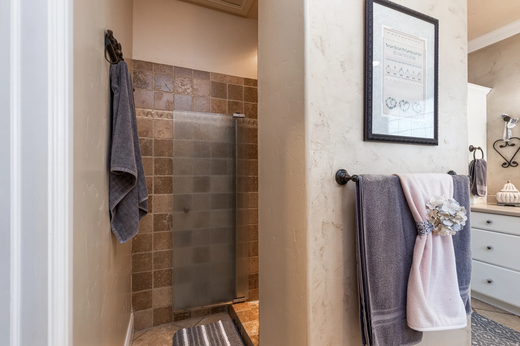 Tiled shower enclosure with a frosted glass door, complemented by textured wall finishes and crown molding
