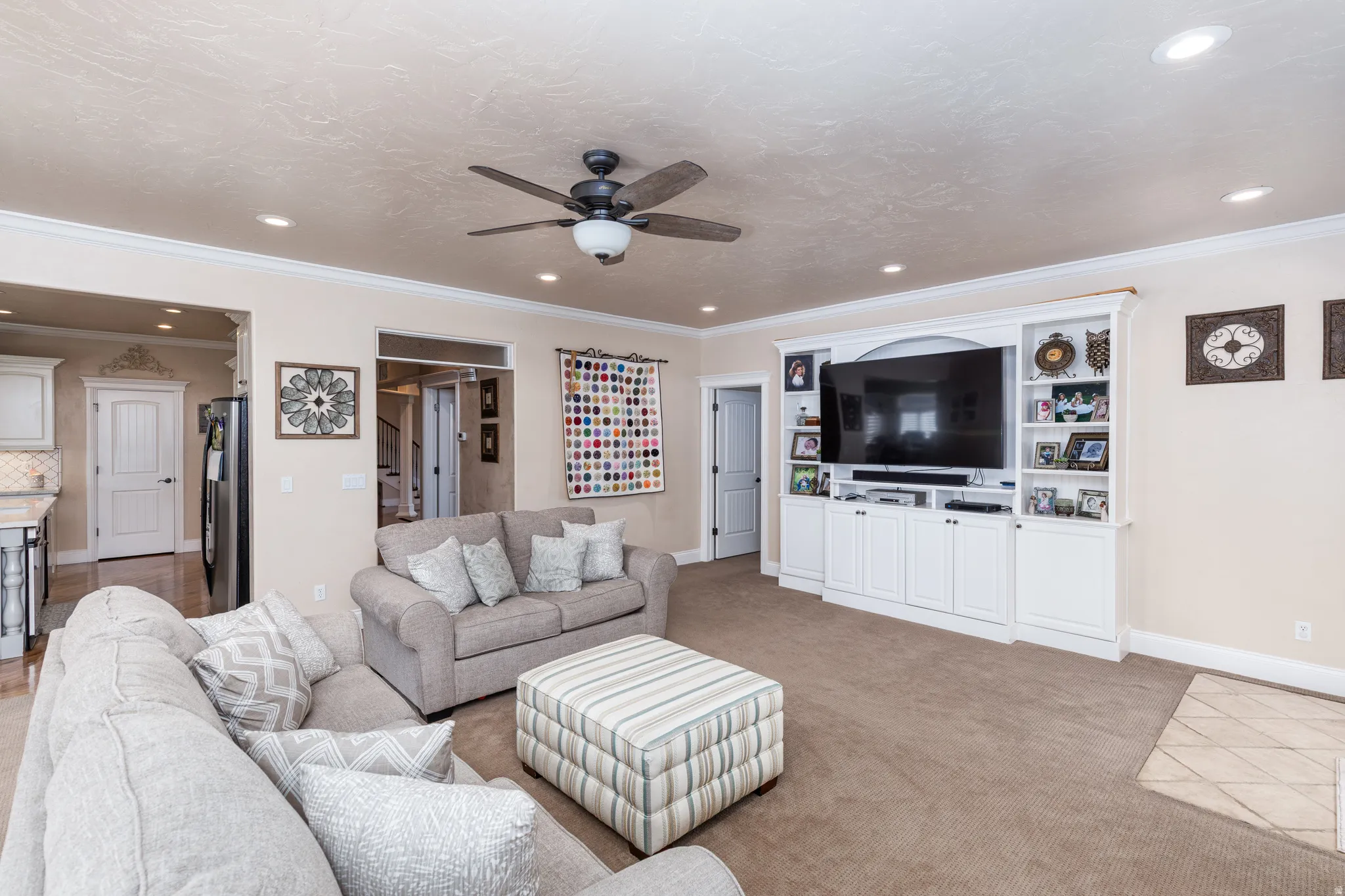 Spacious living area featuring neutral carpeting, recessed lighting, crown molding, a ceiling fan, and a built-in entertainment center with white cabinetry