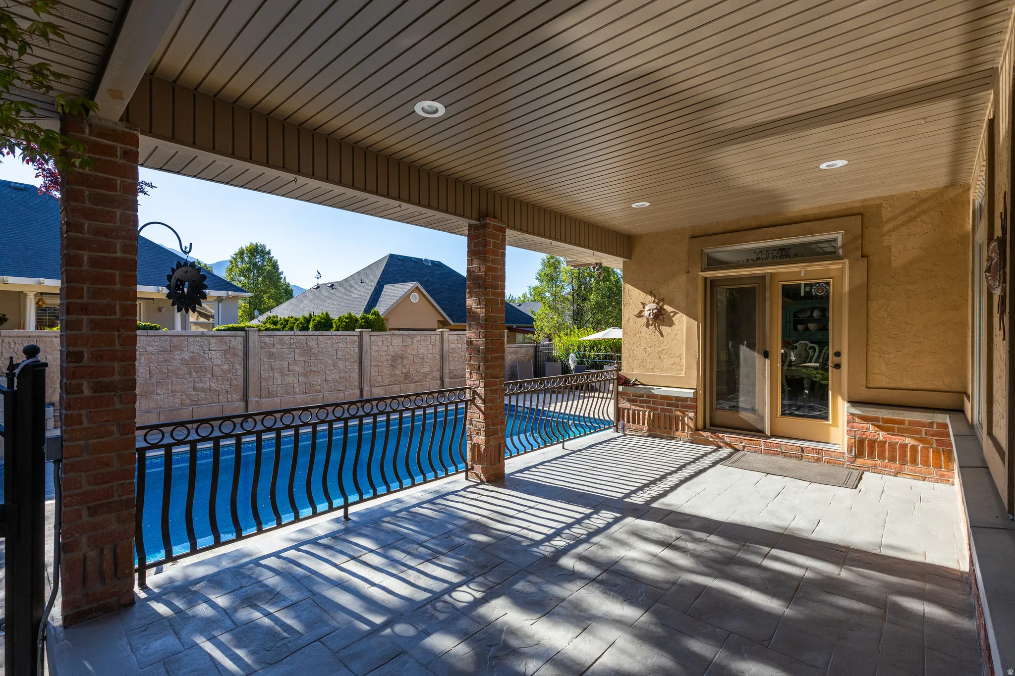 Covered patio with stamped concrete flooring, recessed lighting, brick pillars, wrought iron railing, and direct access to an outdoor pool