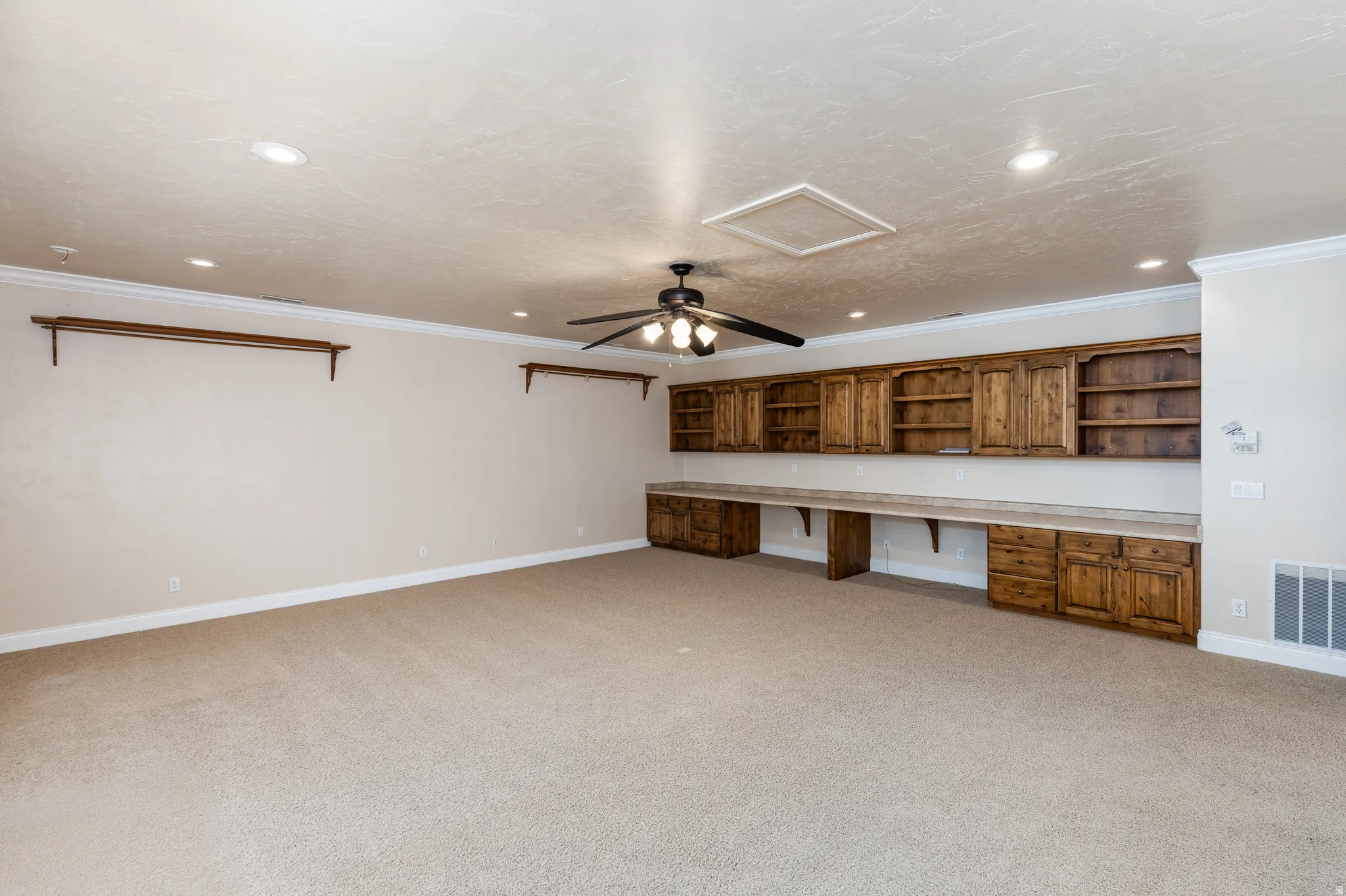 Spacious room featuring extensive built-in wooden cabinetry, integrated desk space, recessed ceiling lighting, a ceiling fan, and light-toned carpeting