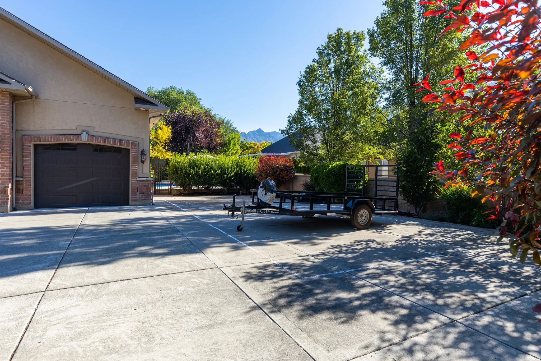 Expansive concrete driveway featuring a brick and stucco exterior, arched garage door, and mature landscaping