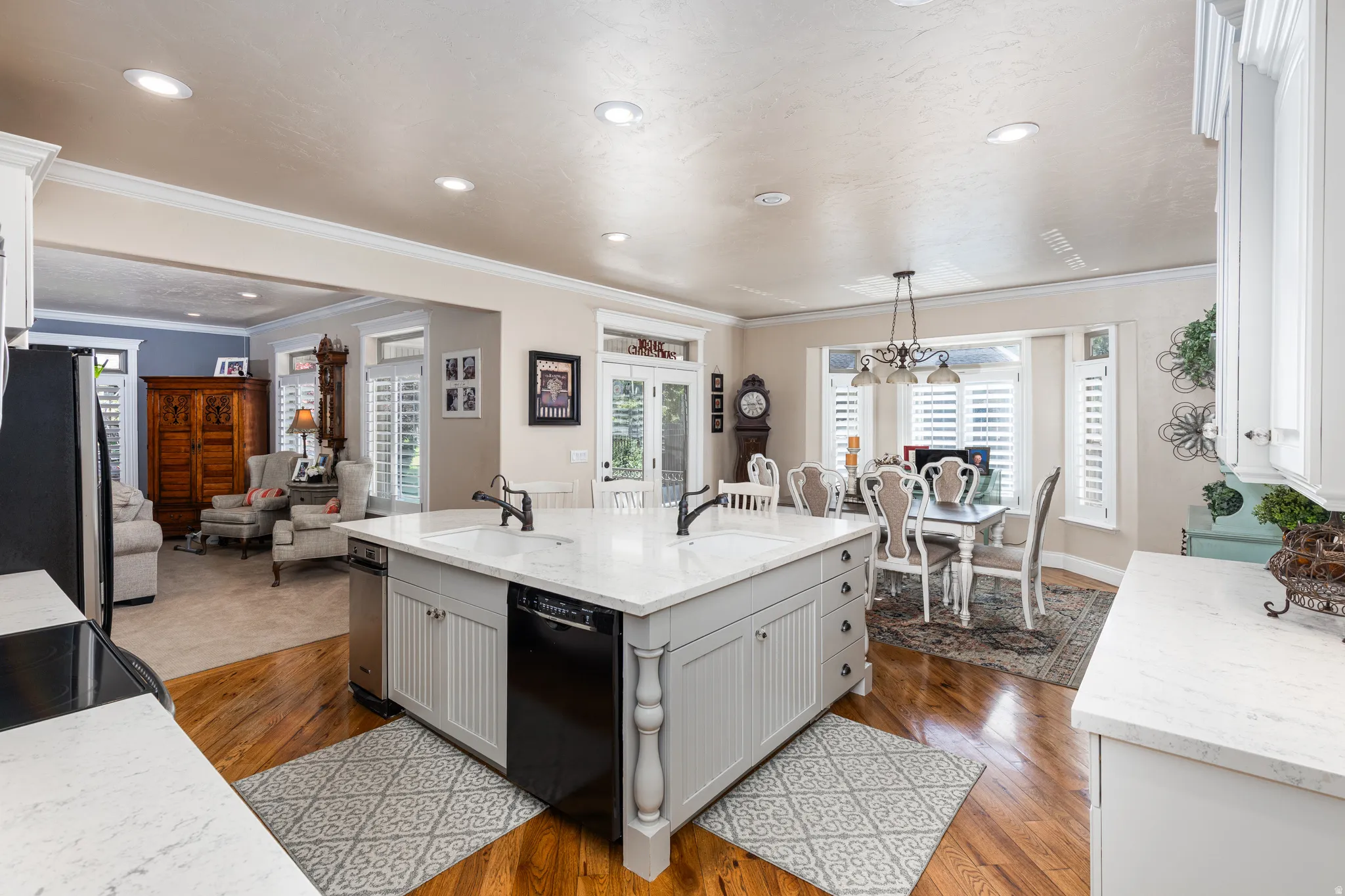 Open-concept kitchen featuring a spacious island with a sink and integrated dishwasher, light-toned countertops, white cabinetry, and wood-finish flooring