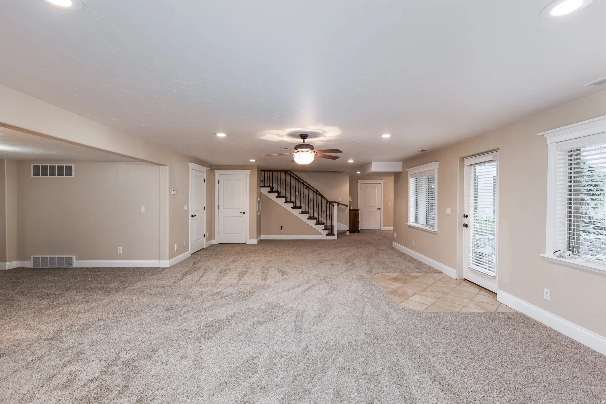 Spacious open area featuring neutral-toned carpeting, recessed lighting, and a ceiling fan