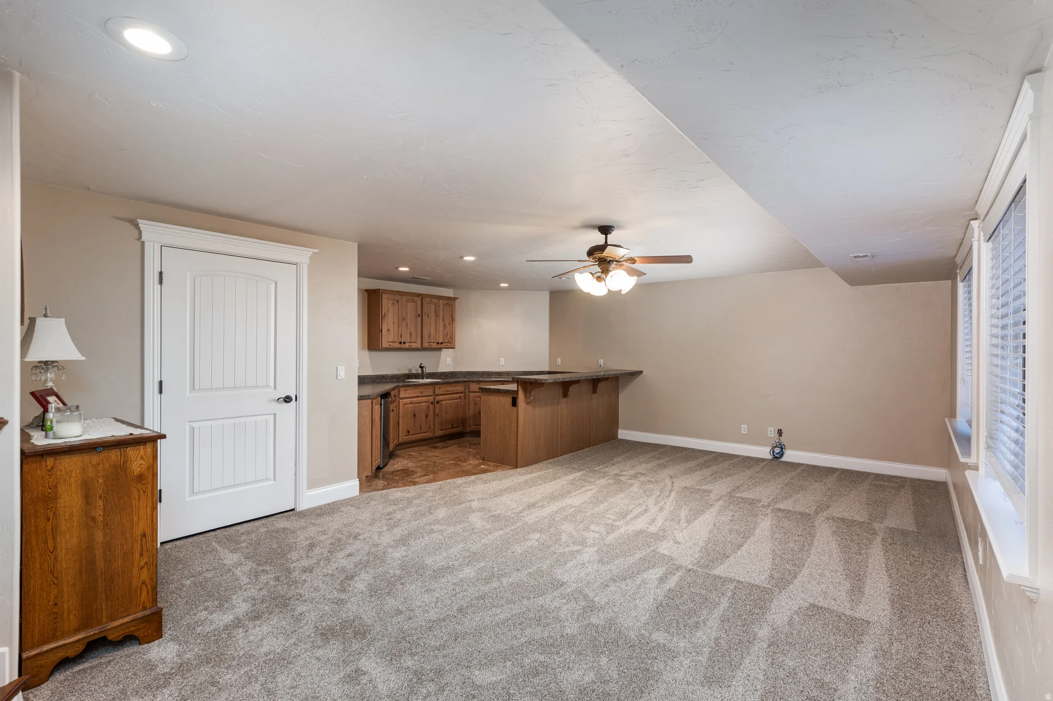 Spacious room featuring a built-in wet bar with wood cabinetry, a ceiling fan, recessed lighting, and two windows with blinds