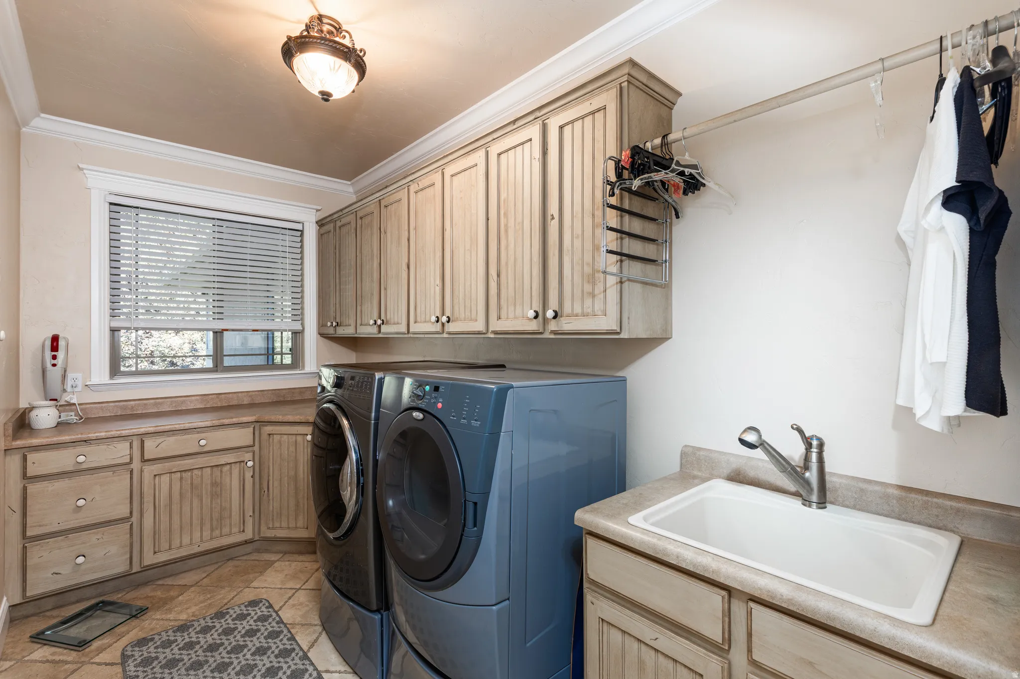 Functional laundry room featuring extensive cabinetry, durable countertop surfaces, an integrated sink, and a hanging rod for convenience