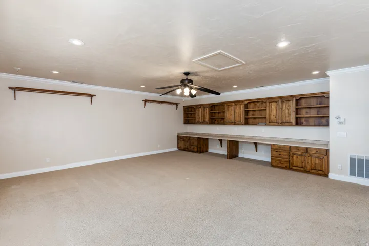 Spacious room featuring extensive built-in wooden cabinetry, integrated desk space, recessed ceiling lighting, a ceiling fan, and light-toned carpeting