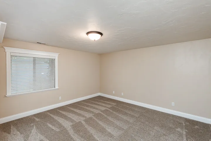 Spacious room featuring neutral paint, textured ceiling, patterned carpet, and a window with white trim and blinds