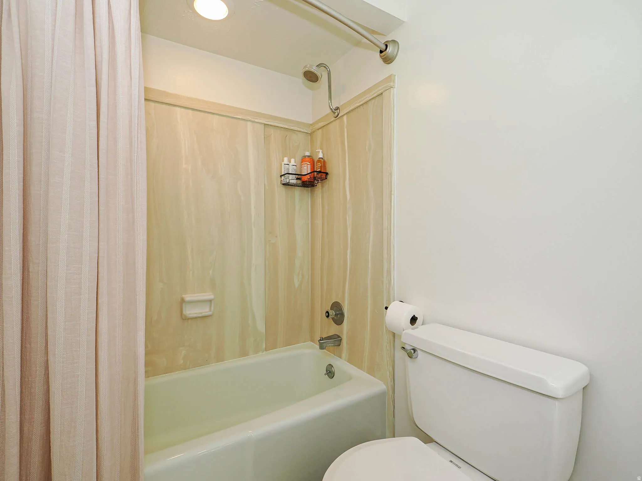 White bathtub with a chrome shower fixture, surrounded by light-toned, vertically paneled shower walls