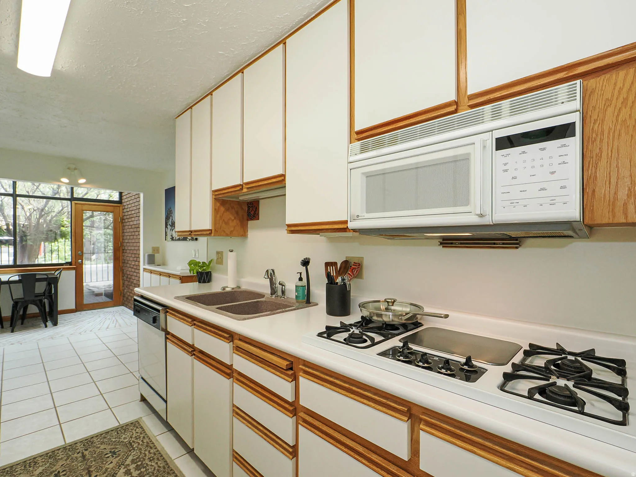 Kitchen featuring white cabinetry with wood trim, a built-in microwave, a gas cooktop, a double basin sink, and white tile flooring