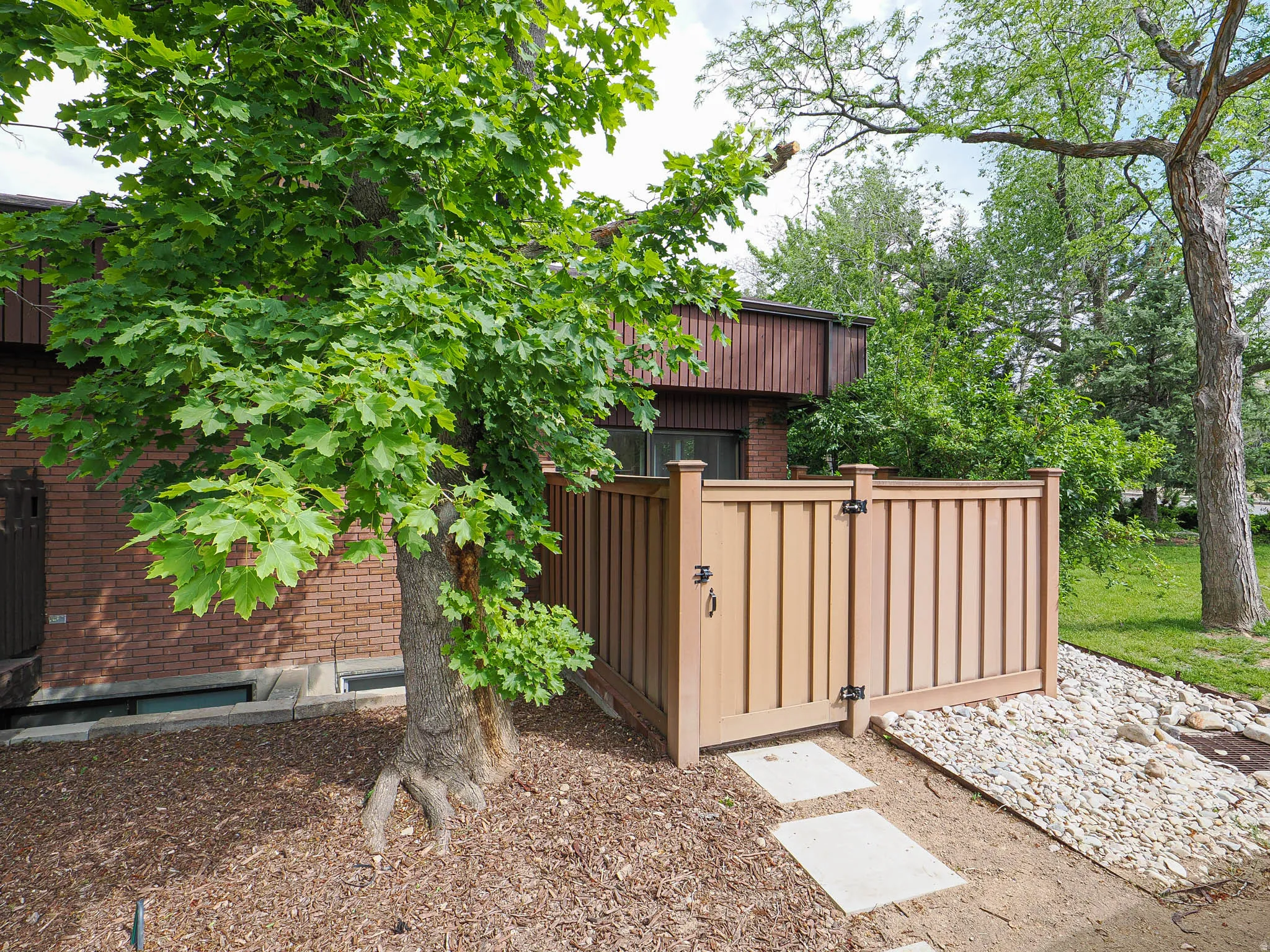 Private outdoor area featuring a tall privacy fence with a gate, concrete stepping stones, and a mulched garden bed