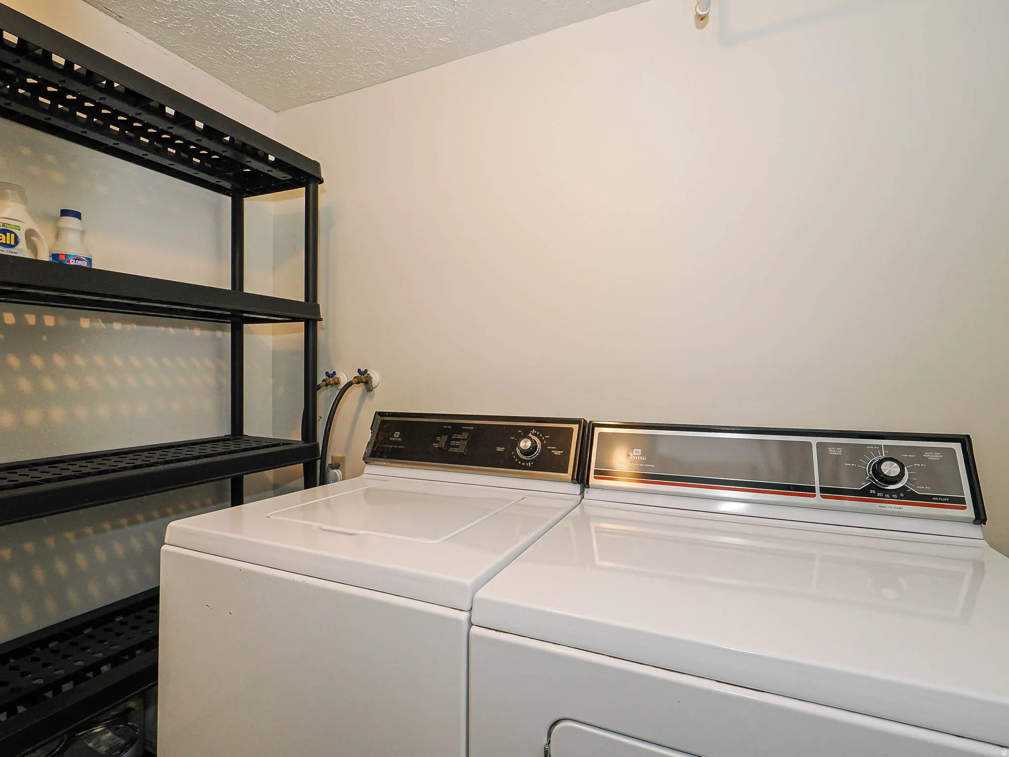 Dedicated laundry space featuring a washer and dryer, accompanied by a black shelving unit for storage