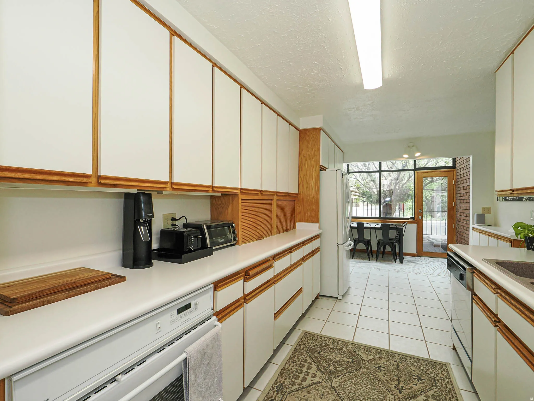 Kitchen featuring extensive white cabinetry with wood trim, white countertops, tile flooring, and integrated appliances
