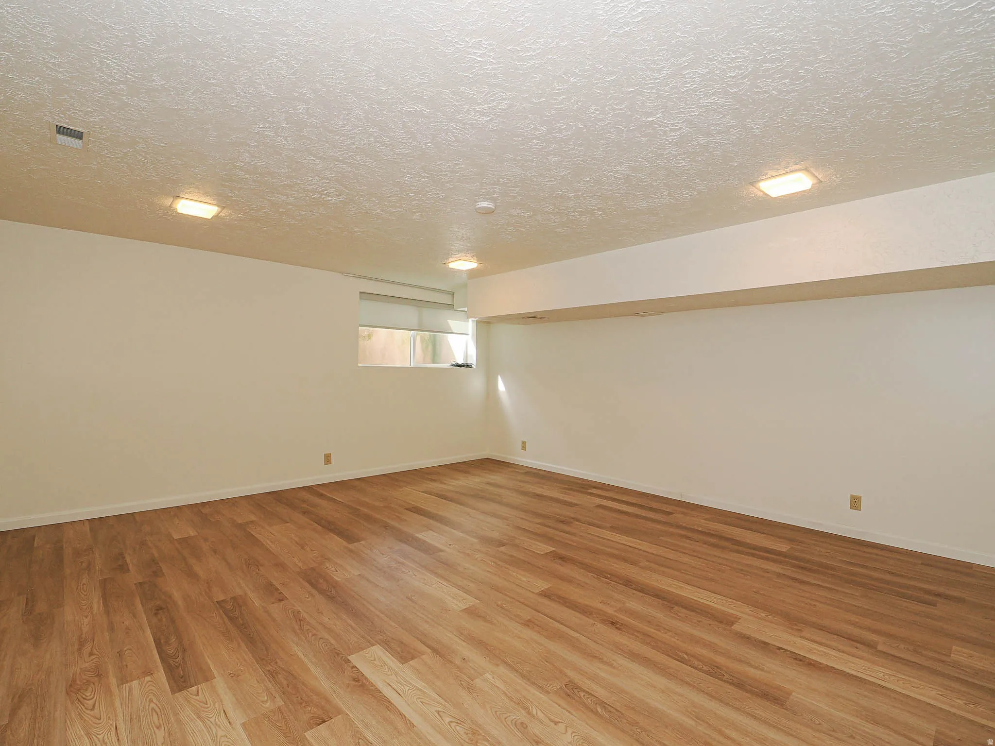 Spacious room featuring light wood-finish flooring, neutral wall tones, and recessed ceiling lighting
