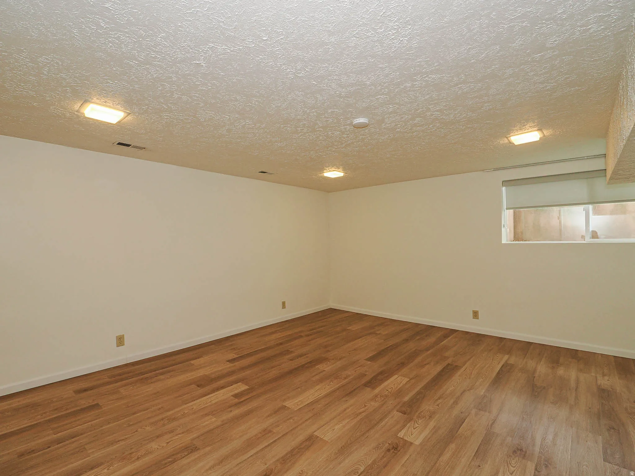 Spacious room featuring wood-finish flooring, white walls, and a textured white ceiling