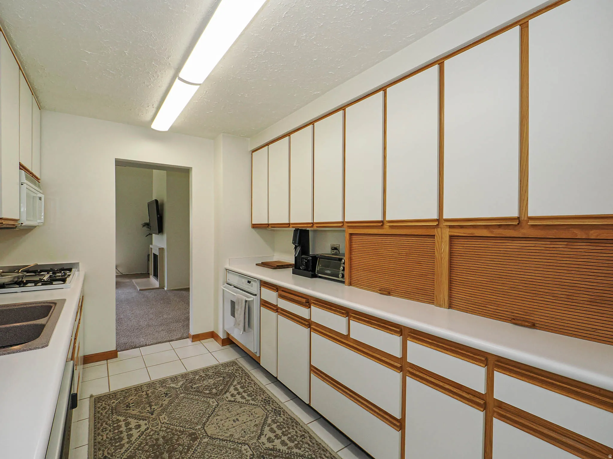 Galley kitchen featuring extensive white cabinetry with wood trim, white countertops, tile flooring, a built-in gas range, and a dual basin sink