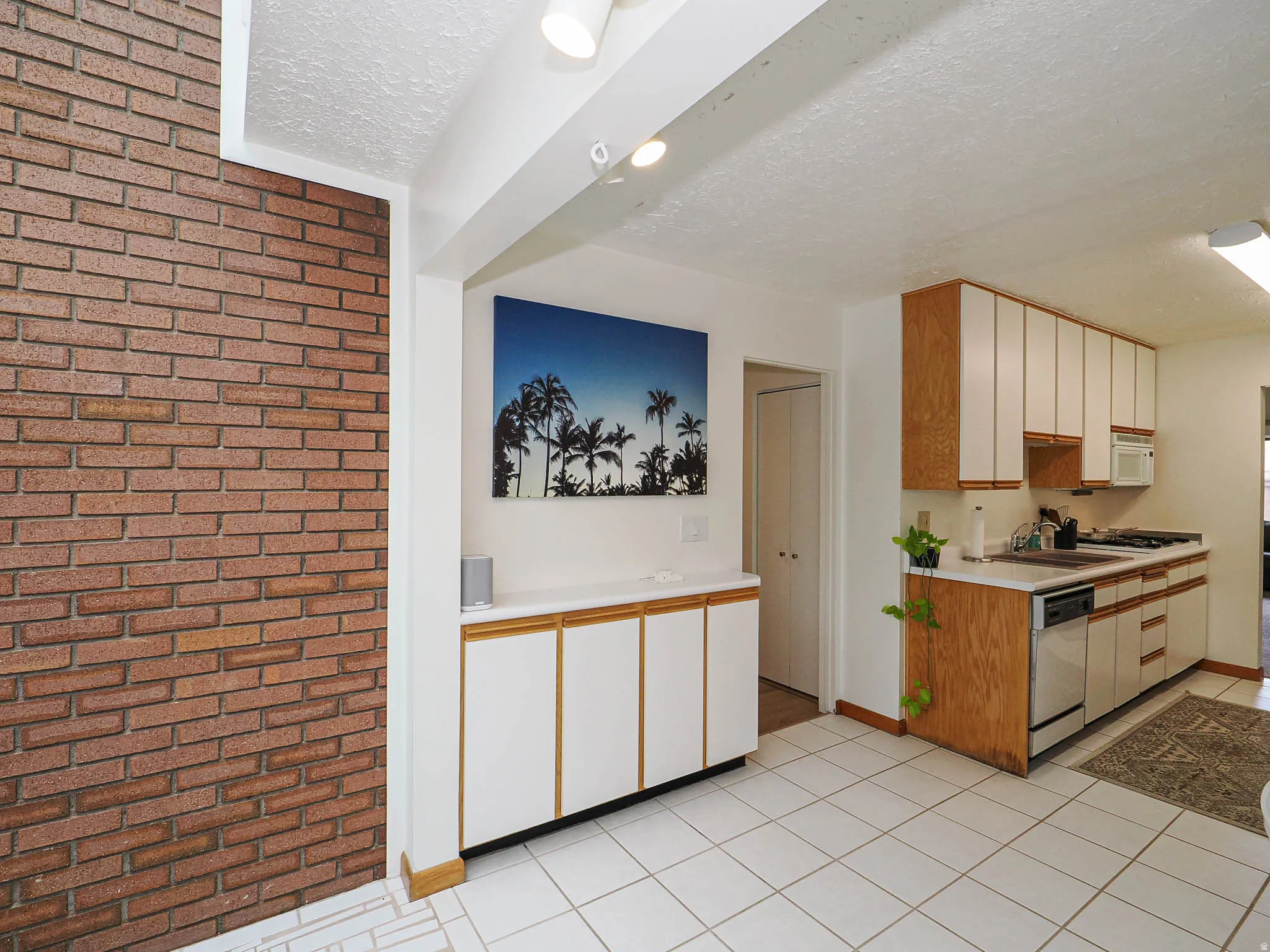 Kitchen featuring white tile flooring, wood-finish cabinetry with white panel doors, and stainless steel appliances