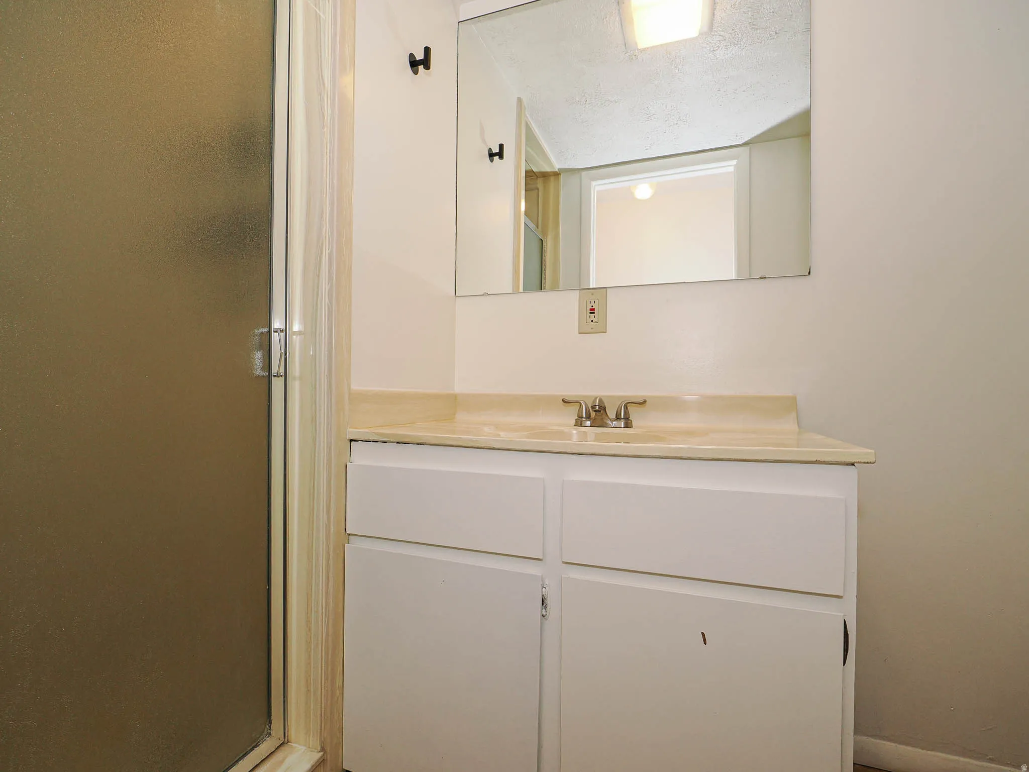Bathroom vanity featuring a light-toned countertop with integrated sink, white cabinetry with two doors and two drawers, and a wall-mounted mirror