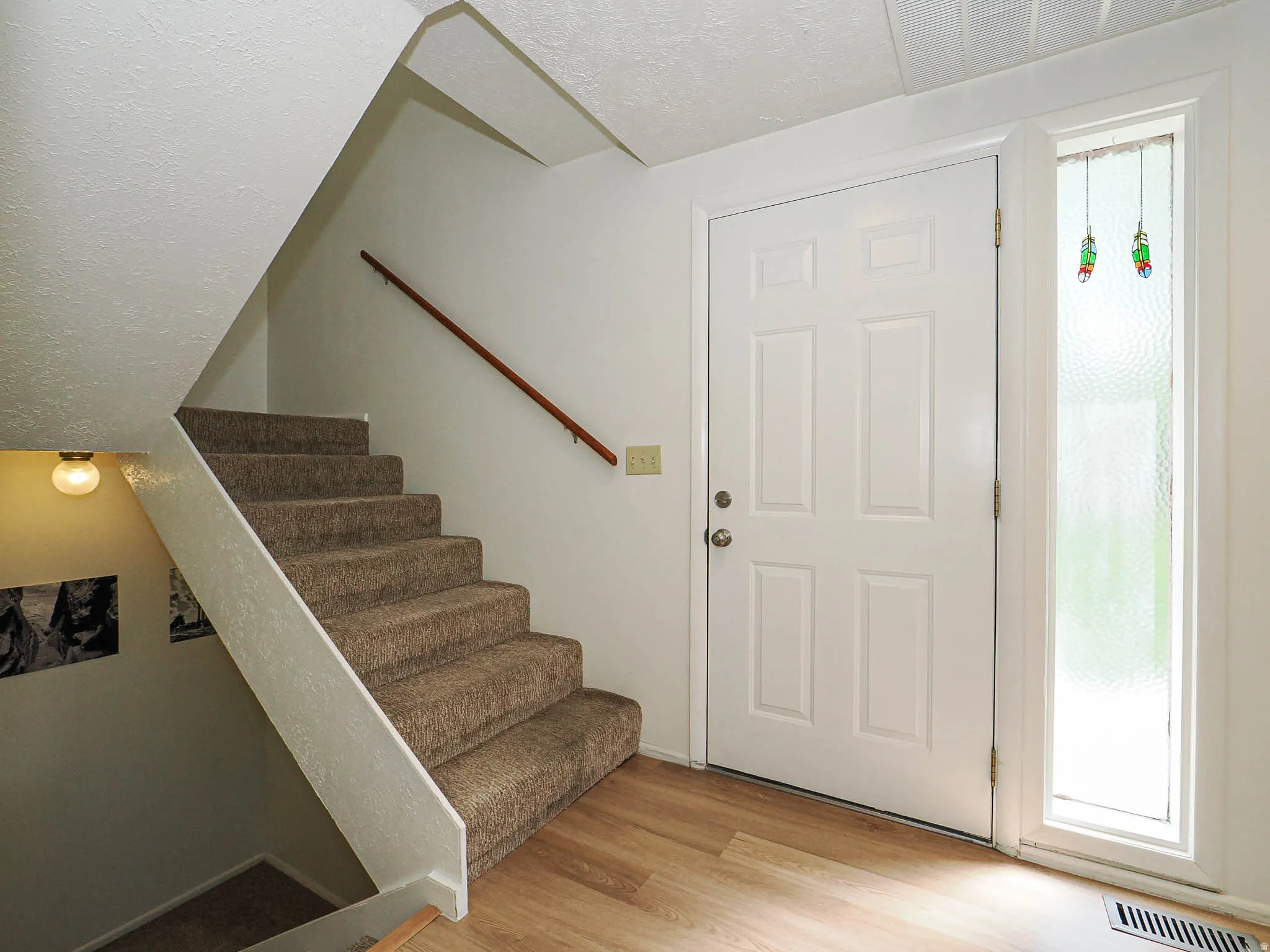 Entryway featuring a paneled door with a sidelight, wood-finish flooring, and a carpeted staircase with a wood handrail