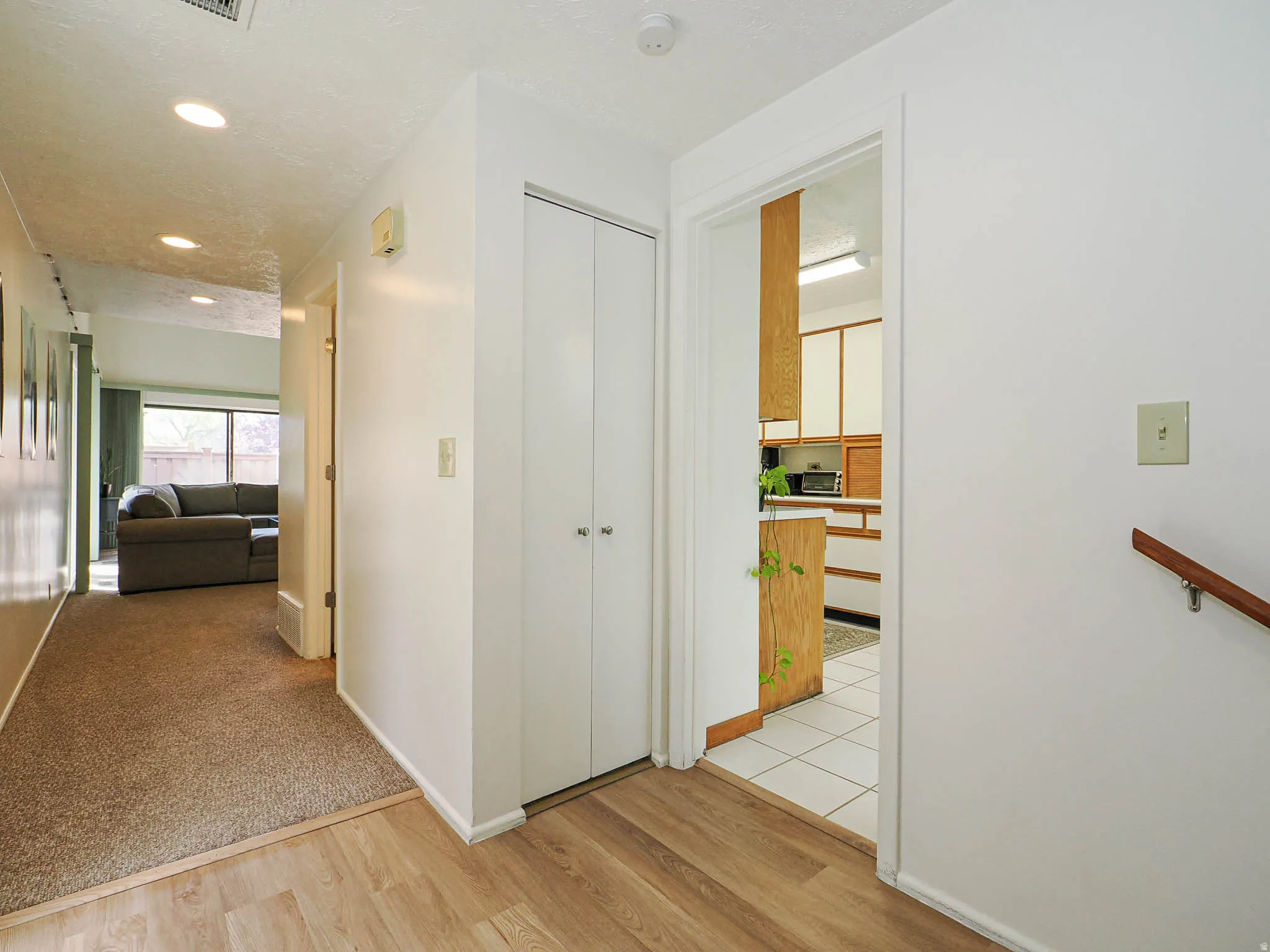 Hallway with wood-finish flooring transitioning to carpet, featuring a built-in closet with bifold doors, and recessed ceiling lighting
