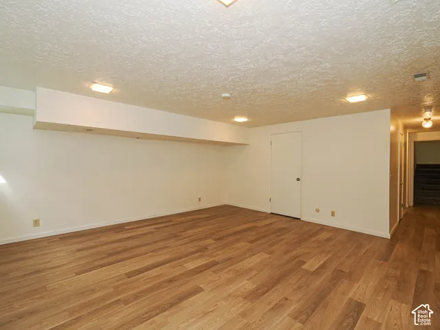 Spacious room featuring wood-finish flooring, white walls, and flush-mount ceiling lighting