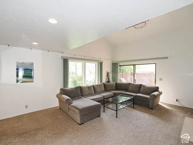 Living area featuring vaulted ceilings, recessed lighting, carpet flooring, a large sliding glass door, and additional windows