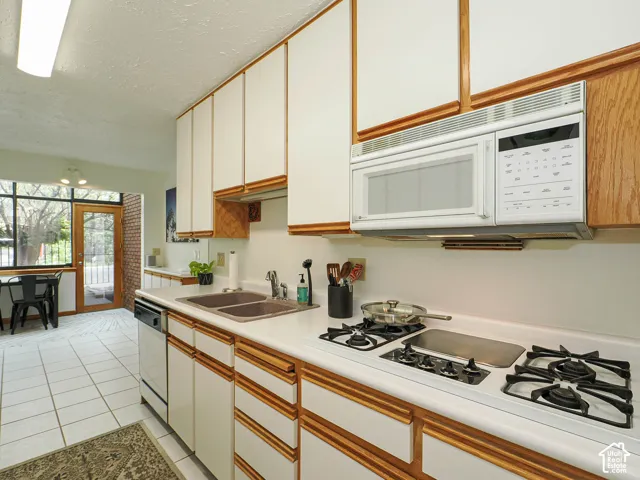 Kitchen featuring white cabinetry with wood trim, a built-in microwave, a gas cooktop, a double basin sink, and white tile flooring
