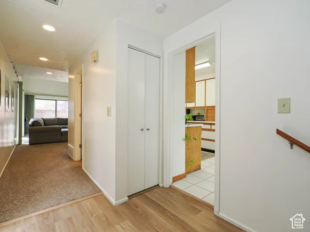 Hallway with wood-finish flooring transitioning to carpet, featuring a built-in closet with bifold doors, and recessed ceiling lighting