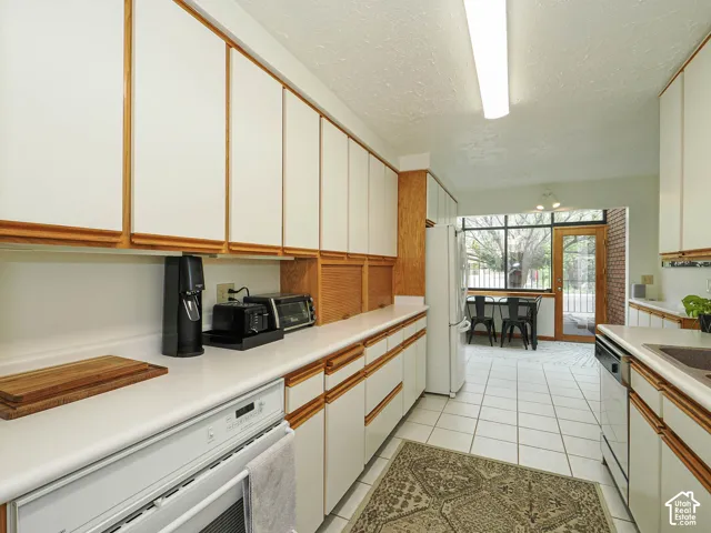 Kitchen featuring extensive white cabinetry with wood trim, white countertops, tile flooring, and integrated appliances
