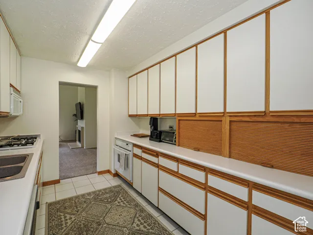 Galley kitchen featuring extensive white cabinetry with wood trim, white countertops, tile flooring, a built-in gas range, and a dual basin sink