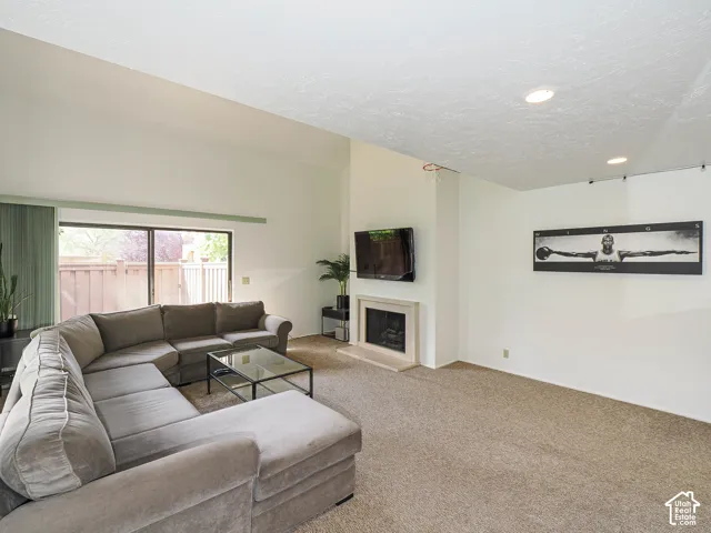 Living area featuring a fireplace with a light-toned surround, a high vaulted ceiling, recessed lighting, and sliding glass doors opening to the exterior
