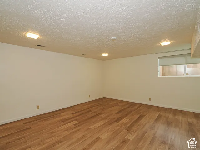 Spacious room featuring wood-finish flooring, white walls, and a textured white ceiling