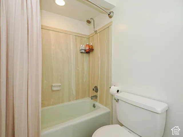 White bathtub with a chrome shower fixture, surrounded by light-toned, vertically paneled shower walls