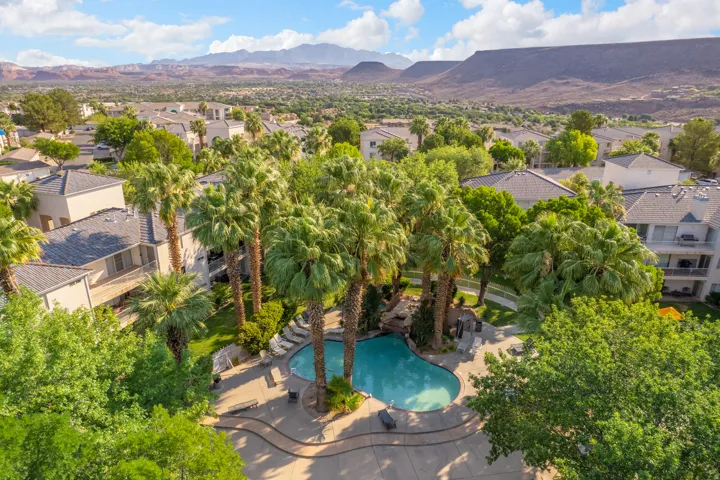 Resort-style pool area featuring mature palm trees, a rock waterfall, and integrated sun decks