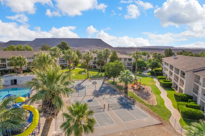 Community amenities featuring an outdoor swimming pool, a multi-sport court with basketball hoops and pickleball lines, and a playground area, all surrounded by mature palm trees and green landscaping