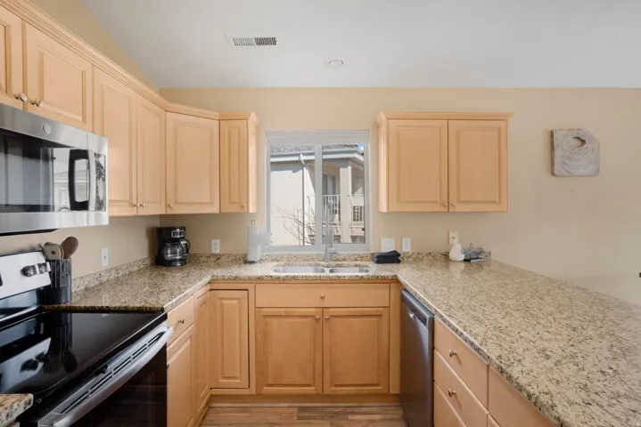 U-shaped kitchen featuring light wood cabinetry and granite-style countertops